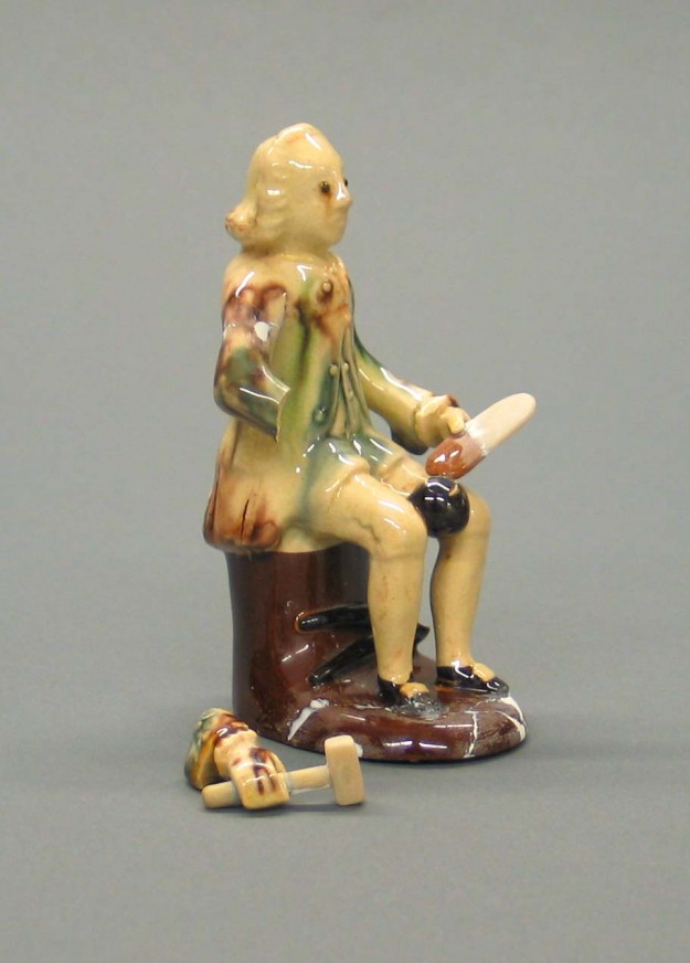 A ceramic figurine of a man sitting on top of a tree stump.