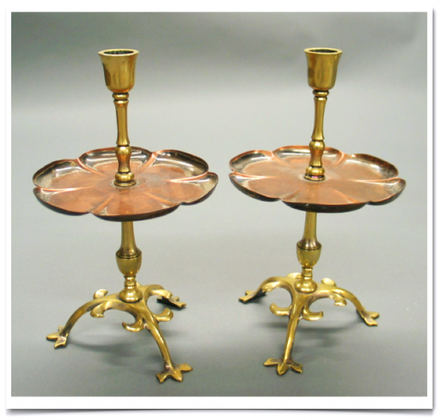 A pair of brass candlesticks with copper plates.